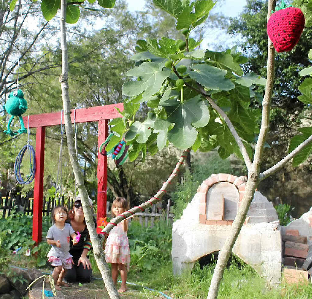 YARN BOMBED: Max Burgess (centre) with her son Juno and neighbour Kahula Dangerfield at the Little Keen St community garden that had a surprise visit from some yarn guerrillas on Sunday night. YARN BOMBED: Max Burgess (centre) with her son Juno and neighbour Kahula Dangerfield at the Little Keen St community garden that had a surprise visit from some yarn guerrillas on Sunday night.
