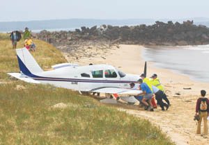 Police and volunteers push the grounded Piper Cherokee away from the rising tide yesterday. Police and volunteers push the grounded Piper Cherokee away from the rising tide yesterday.