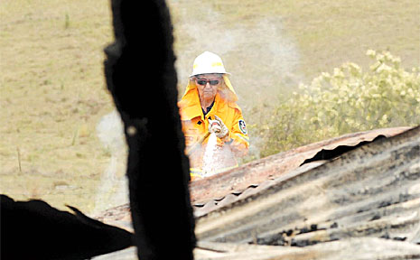 NSW Rural Fire Brigades volunteer Rita Pomroy sprays water on the smouldering remains of the cottage. NSW Rural Fire Brigades volunteer Rita Pomroy sprays water on the smouldering remains of the cottage.