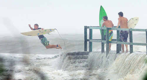 A thrill-seeker leaps into turbulent surf from the jetty at Fisherman’s Beach at Emu Park, grateful for the extreme weather that has closed roads, uprooted trees and caused flooding throughout the region. A thrill-seeker leaps into turbulent surf from the jetty at Fisherman’s Beach at Emu Park, grateful for the extreme weather that has closed roads, uprooted trees and caused flooding throughout the region.