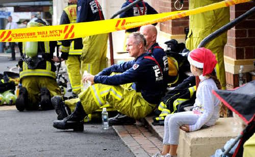 Sophie Ward, 5, sits behind the fire tape in Byron Street, Bangalow, near firefighters taking a break from fighting the blaze. Sophie Ward, 5, sits behind the fire tape in Byron Street, Bangalow, near firefighters taking a break from fighting the blaze.