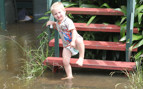 Two-year-old Zaidan departs his Lakes Creek Road home as water laps the steps yesterday Two-year-old Zaidan departs his Lakes Creek Road home as water laps the steps yesterday