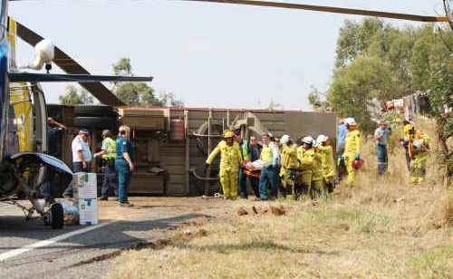 Emergency services carry the male driver of the truck wreck (background) to the RACQ Capricorn Rescue chopper. Emergency services carry the male driver of the truck wreck (background) to the RACQ Capricorn Rescue chopper.