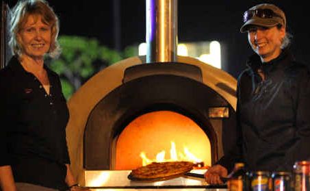 Helen Stewart and Fiona Howard from Pizza Under Fire cook a pizza in their wood-fired oven.