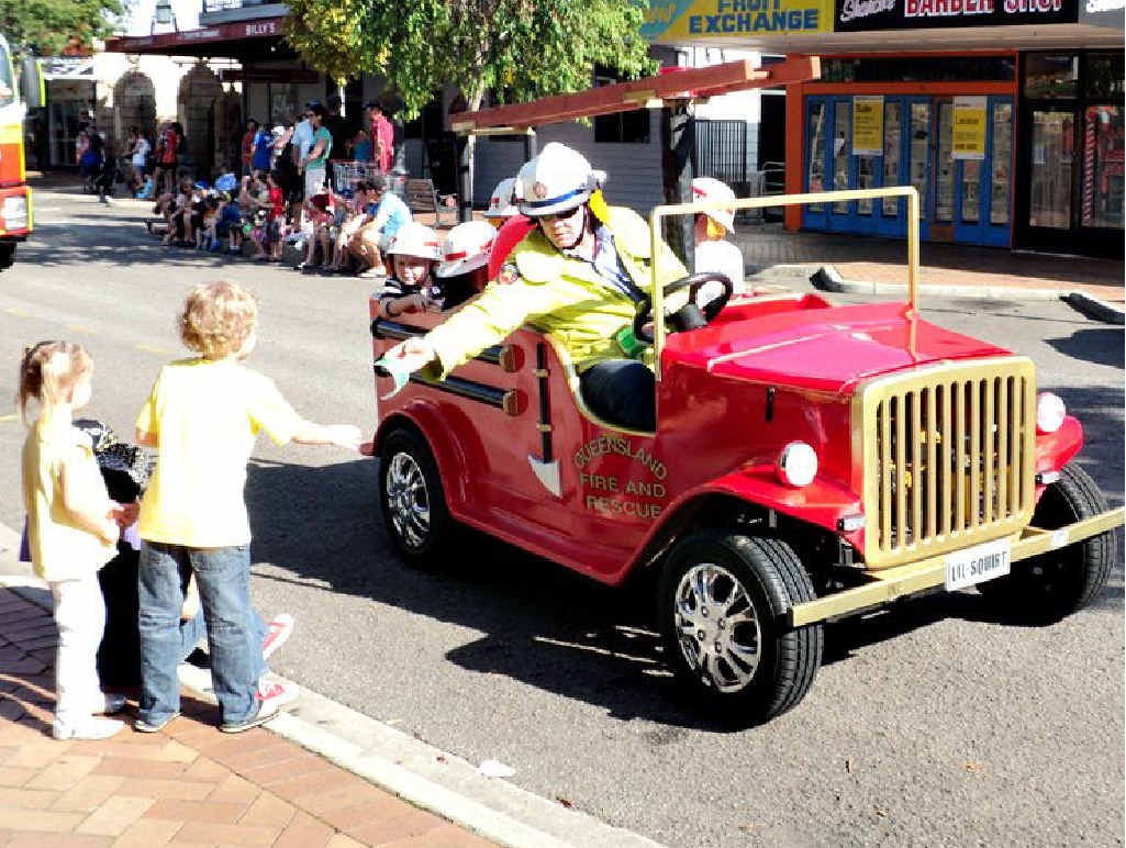 A firefighter from Gympie Fire and Rescue hands out stickers from his miniature vintage fire truck to young spectators in the Gold Rush Parade.