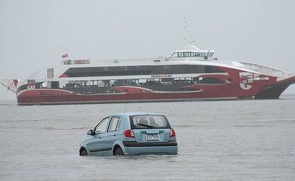 The Big Red Cat sails past the tourists' car. The low tide and a GPS navigation system lured them into the bay at Oyster Point at Cleveland. The Big Red Cat sails past the tourists' car. The low tide and a GPS navigation system lured them into the bay at Oyster Point at Cleveland.