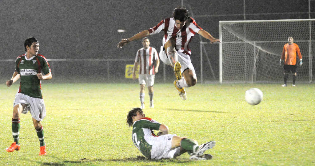Lion’s Daniel Allen hurdles a Strikers player as he slides in for a tackle in the rain Saturday night. Lion’s Daniel Allen hurdles a Strikers player as he slides in for a tackle in the rain Saturday night.