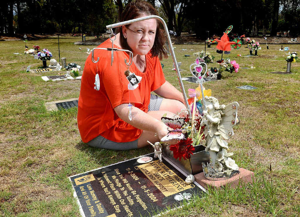 SHATTERED: Mary Beck at her daughter’s grave at Warrill Park Lawn Cemetery. Mary is upset that the cemetery staff have placed letters on graves asking for all trinkets to be removed. SHATTERED: Mary Beck at her daughter’s grave at Warrill Park Lawn Cemetery. Mary is upset that the cemetery staff have placed letters on graves asking for all trinkets to be removed.