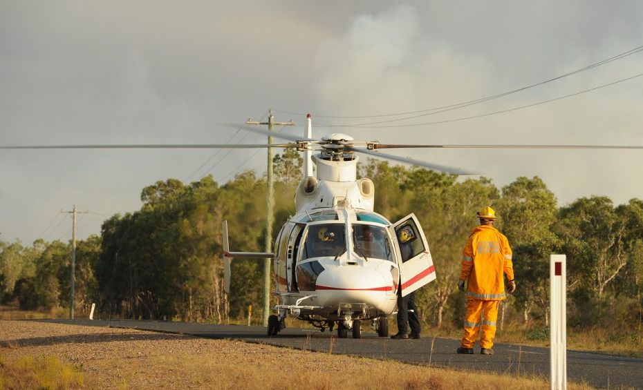A firefighter guides the pilot of a helicopter to land on the Boonooroo Road to pick up a fire supervisor to monitor the blaze from the air. A firefighter guides the pilot of a helicopter to land on the Boonooroo Road to pick up a fire supervisor to monitor the blaze from the air.