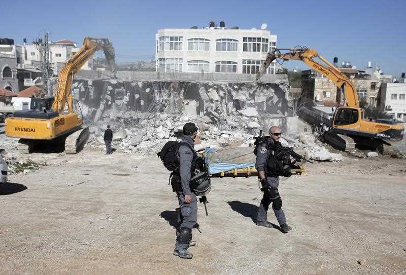Members of the Israeli security forces stand guard as bulldozers hired by the Jerusalem municipality destroy a Palestinian house in the Israeli annexed East Jerusalem neighbourhood of Shuafat on January 21, 2015, on the grounds that it was built without a construction permit. Palestinian homes built without a construction permit are often demolished by order of the Jerusalem municipality. Members of the Israeli security forces stand guard as bulldozers hired by the Jerusalem municipality destroy a Palestinian house in the Israeli annexed East Jerusalem neighbourhood of Shuafat on January 21, 2015, on the grounds that it was built without a construction permit. Palestinian homes built without a construction permit are often demolished by order of the Jerusalem municipality.