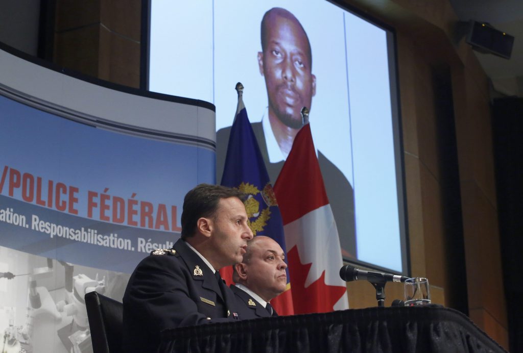 Royal Canadian Mounted Police assistant commissioner James Malizia, left, and Inspector Paul Mellon speak at a press conference at RCMP headquarters in Ottawa, Ontario, about the arrest of a Somali man Ali Omar Ader, shown on the screen, for his involvement in the kidnapping of Canadian journalist Amanda Lindhout and Australian photojournalist Nigel Brennan, Friday, June 12, 2015. (Patrick Doyle/The Canadian Press via AP) MANDATORY CREDIT Royal Canadian Mounted Police assistant commissioner James Malizia, left, and Inspector Paul Mellon speak at a press conference at RCMP headquarters in Ottawa, Ontario, about the arrest of a Somali man Ali Omar Ader, shown on the screen, for his involvement in the kidnapping of Canadian journalist Amanda Lindhout and Australian photojournalist Nigel Brennan, Friday, June 12, 2015. (Patrick Doyle/The Canadian Press via AP) MANDATORY CREDIT