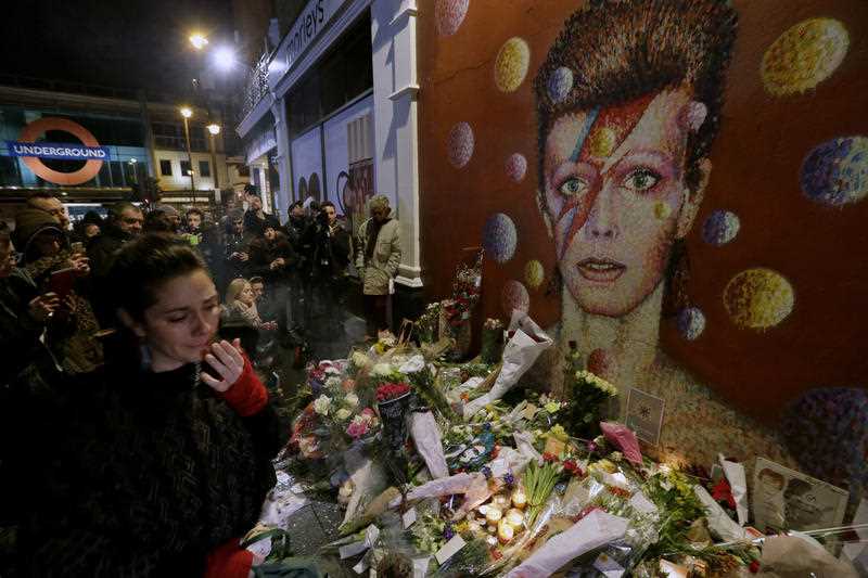 People gather next to tributes placed near a mural of British singer David Bowie by artist Jimmy C, in Brixton, south London, Monday, Jan. 11, 2016. Bowie, the other-worldly musician who broke pop and rock boundaries with his creative musicianship, nonconformity, striking visuals and a genre-spanning persona he christened Ziggy Stardust, died of cancer Sunday aged 69. He was born in Brixton. People gather next to tributes placed near a mural of British singer David Bowie by artist Jimmy C, in Brixton, south London, Monday, Jan. 11, 2016. Bowie, the other-worldly musician who broke pop and rock boundaries with his creative musicianship, nonconformity, striking visuals and a genre-spanning persona he christened Ziggy Stardust, died of cancer Sunday aged 69. He was born in Brixton.