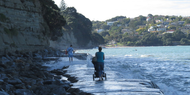 Water starts to lap the woman's feet and her pram as the waves increase in size and ferocity. Photo / Eliane Souza Water starts to lap the woman's feet and her pram as the waves increase in size and ferocity. Photo / Eliane Souza