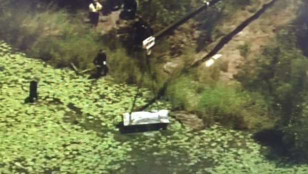 A crane lifts a metal box from a dam at Logan as police search for two bodies. Photo: Nine News Brisbane/Twitter
A crane lifts a metal box from a dam at Logan as police search for two bodies. Photo: Nine News Brisbane/Twitter