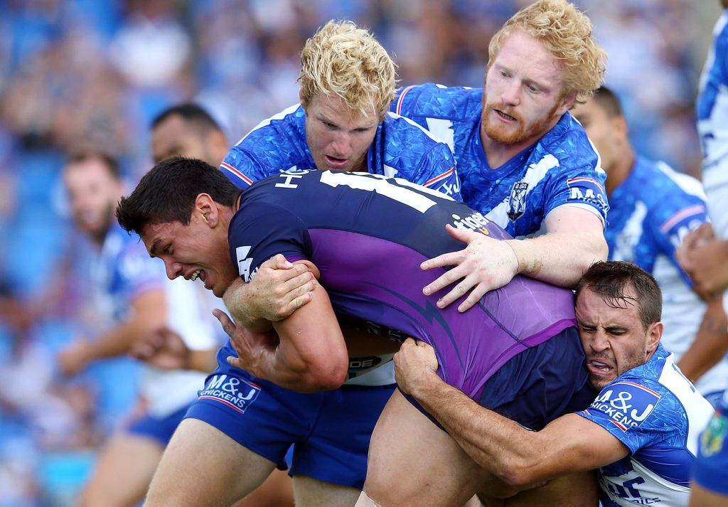 Jordan McLean, of the Storm, is tackled by Aiden Tolman, James Graham and Josh Reynolds, of the Bulldogs, during the NRL Trial match. Photo: Renee McKay/Getty Images. Jordan McLean, of the Storm, is tackled by Aiden Tolman, James Graham and Josh Reynolds, of the Bulldogs, during the NRL Trial match. Photo: Renee McKay/Getty Images.
