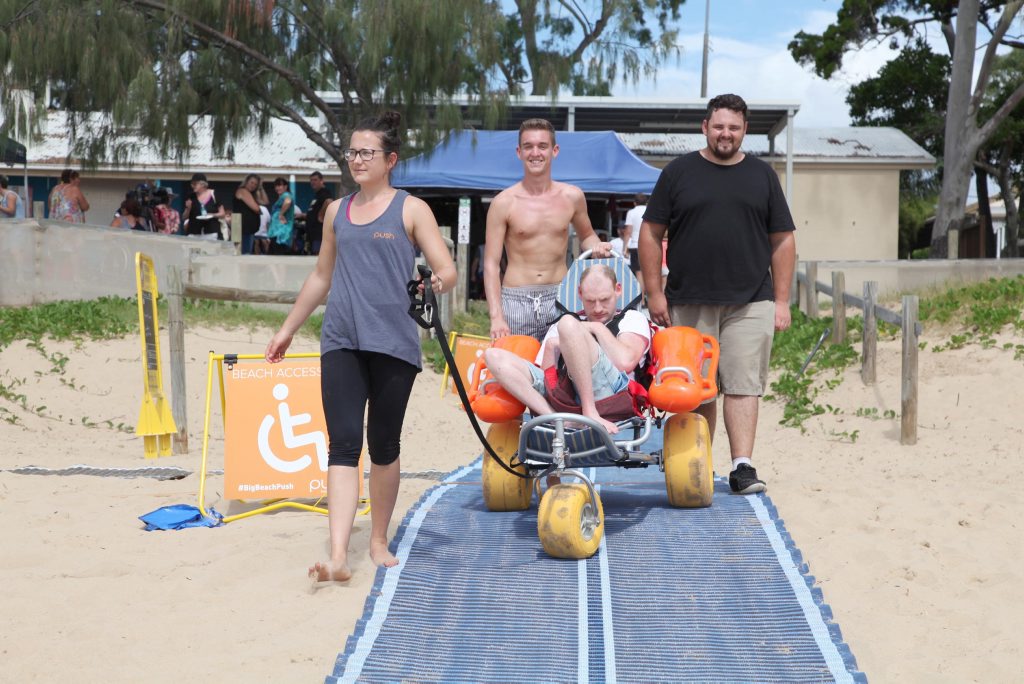 Tony Summerville tries out the Mobi-Mat, assisted by carer Kendrick Lark (right) and Push Mobility's Sian Heaton (left) and James Bean, on Torquay Beach on Sunday. Photo: Jocelyn Watts / Fraser Coast Chronicle Tony Summerville tries out the Mobi-Mat, assisted by carer Kendrick Lark (right) and Push Mobility's Sian Heaton (left) and James Bean, on Torquay Beach on Sunday. Photo: Jocelyn Watts / Fraser Coast Chronicle