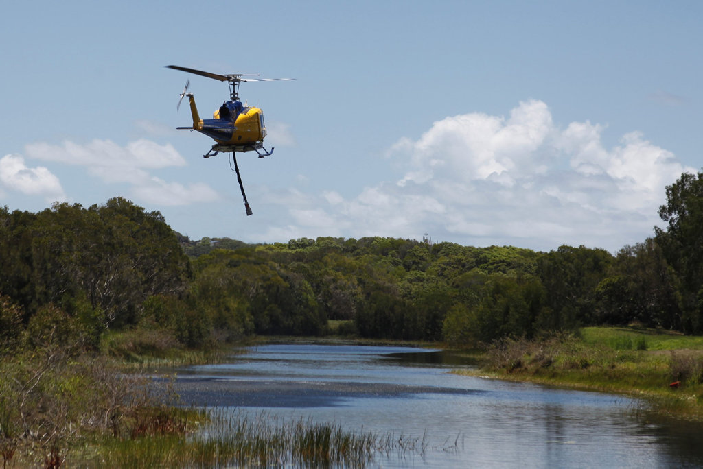 A water bombing helicopter fills up near Mount Coolum before dousing the mountain, as firefighters work to strengthen containment lines.
