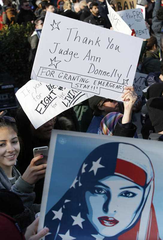 A woman snaps a cell phone photo as others hold up signs acknowledging the federal stay affecting immigrants trying to reach the United States issued by New York federal judge Ann M. Donnelly A woman snaps a cell phone photo as others hold up signs acknowledging the federal stay affecting immigrants trying to reach the United States issued by New York federal judge Ann M. Donnelly